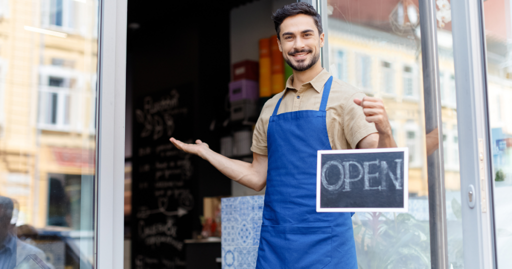 Smiling business owner holding an 'OPEN' sign, representing AFN's flexible cash advances for business growth.