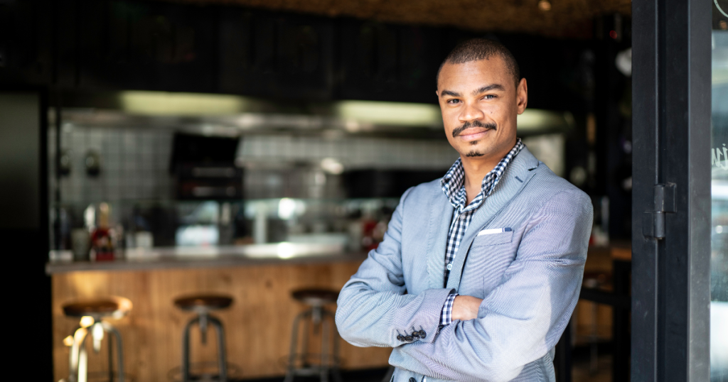 Business owner in a suit standing confidently in a modern cafe, representing growth through Merchant Advance Loans.