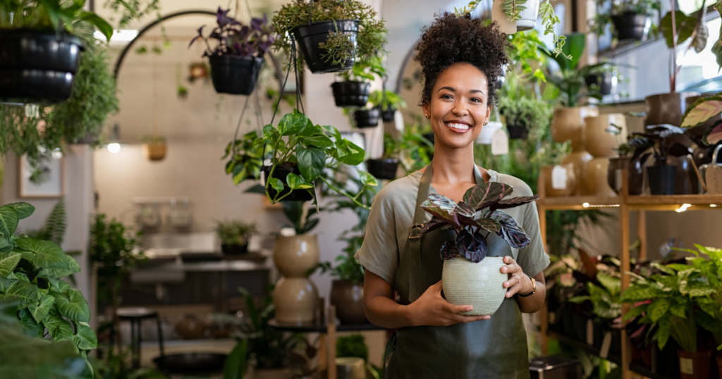 Smiling woman holding a plant in a vibrant garden center, showcasing business line of credit solutions in New Jersey.