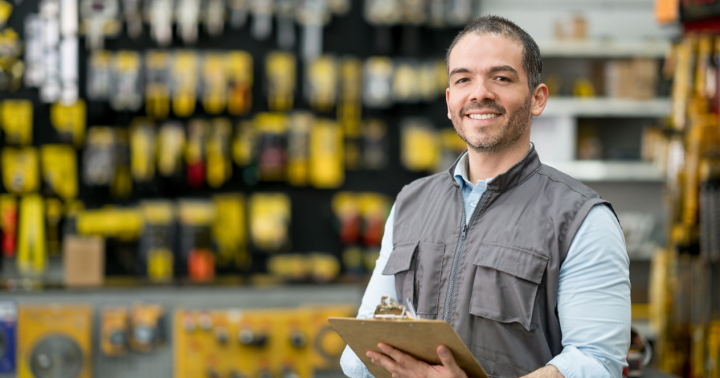 Smiling business owner in a hardware store, showcasing tools and equipment, promoting business cash advances and funding solutions.