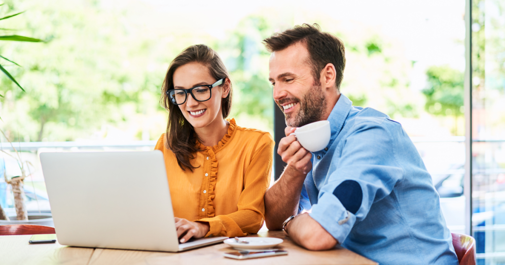 Couple discussing flexible credit options for automotive business financing while using a laptop in a cafe.