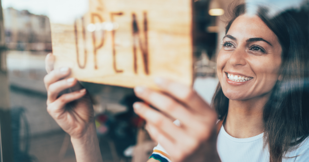 Smiling woman hanging an 'OPEN' sign, representing small business recovery and unsecured credit lines after Hurricane Sandy.