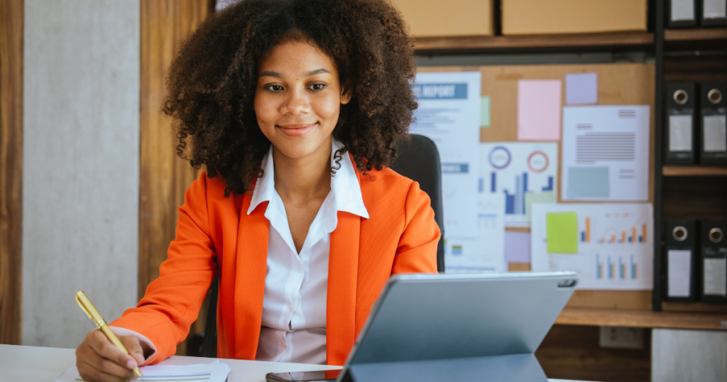 Business professional in an orange blazer managing finances with a tablet, emphasizing receivables financing solutions.