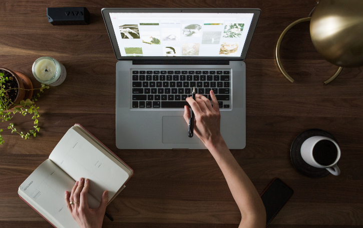 A person working on a laptop with a notebook, coffee, and plants, symbolizing productivity and motivation in challenging economic times.