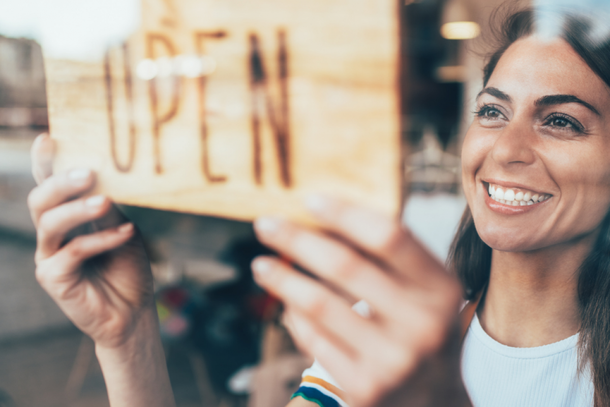 Smiling woman hanging an 'OPEN' sign, representing small business recovery and unsecured credit lines after Hurricane Sandy.