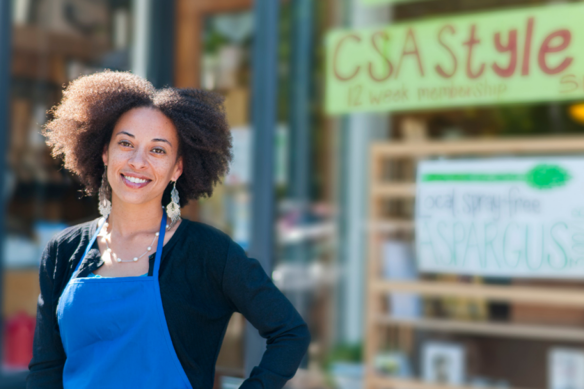 Smiling small business owner in front of a store promoting local produce and holiday shopping strategies.