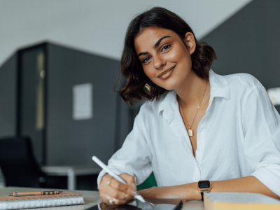 Young entrepreneur smiling while writing notes in a modern office, embodying business success and creativity.