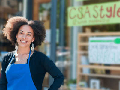 Smiling small business owner in front of a store promoting local produce and holiday shopping strategies.