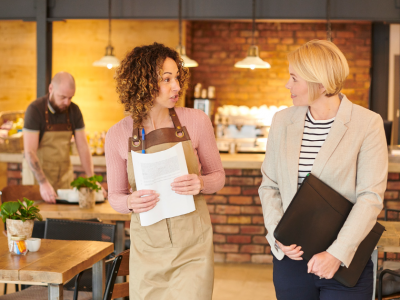 Smiling business owners in aprons discussing unsecured business loans for poor credit applicants in a cafe setting.