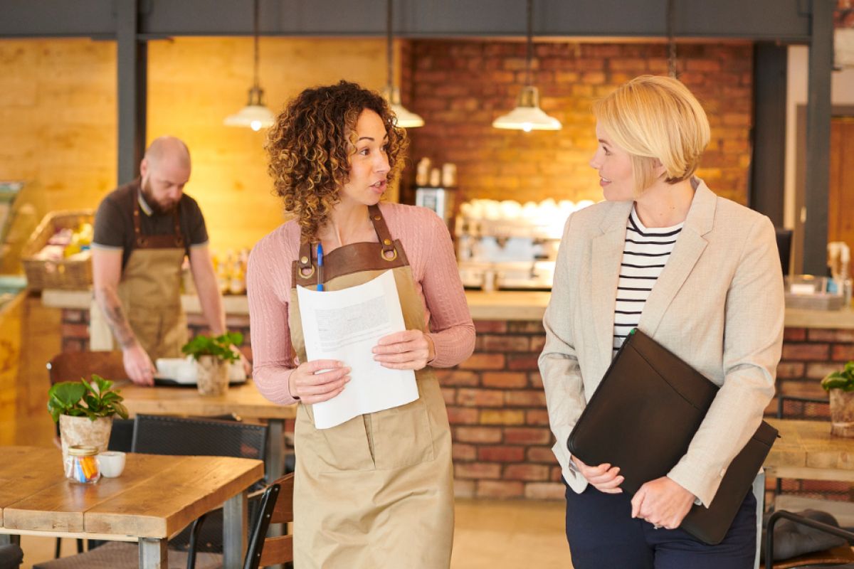 Smiling business owners in aprons discussing unsecured business loans for poor credit applicants in a cafe setting.