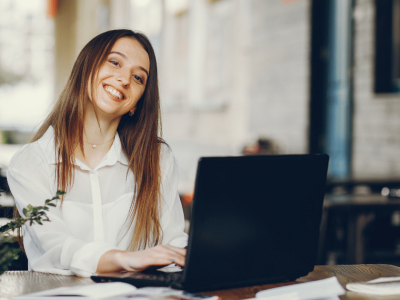 Smiling woman working on a laptop in a cafe, representing social media branding strategies for businesses.