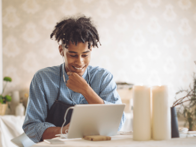 Smiling man using a laptop at a table with candles, representing efficiency in trucking and logistics tools.