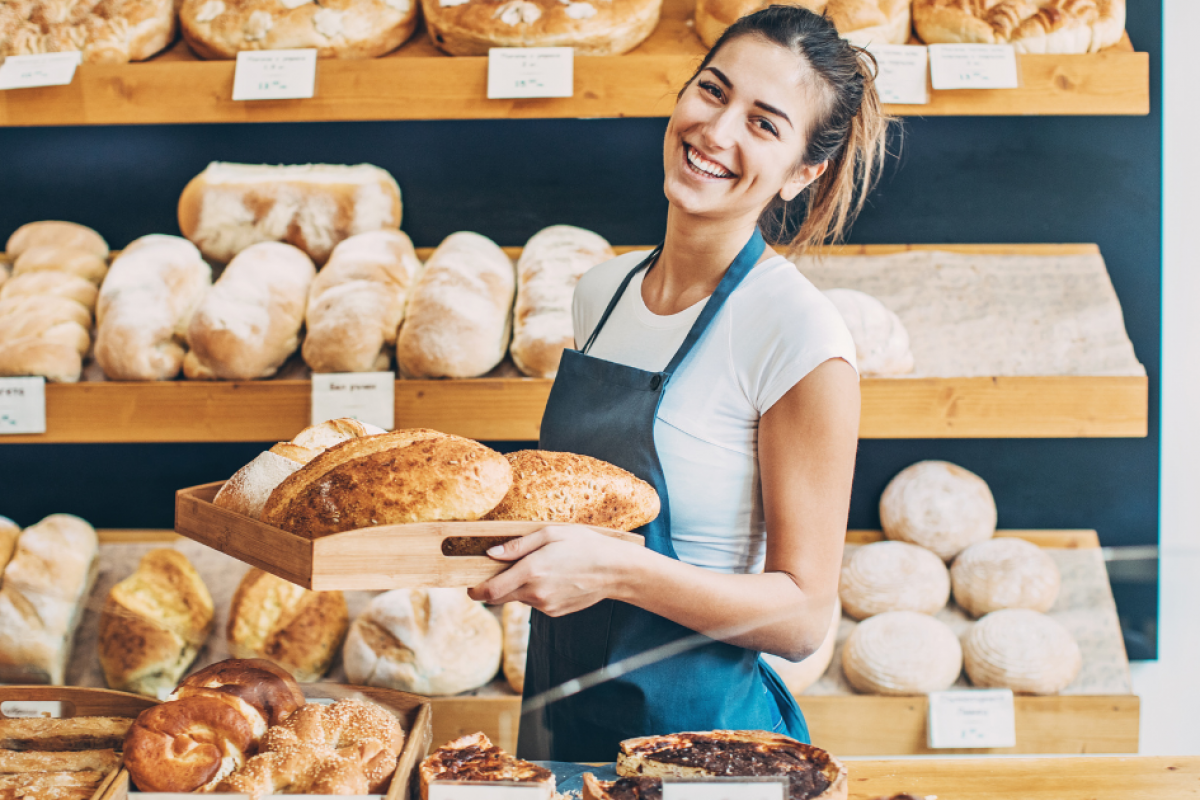 Smiling bakery owner holding fresh bread in a shop, showcasing small business success and growth opportunities.