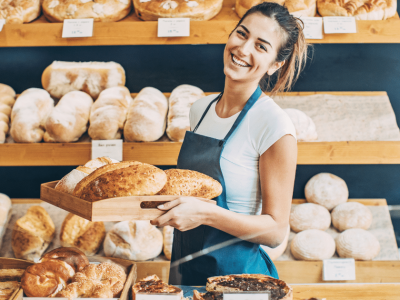 Smiling bakery owner holding fresh bread in a shop, showcasing small business success and growth opportunities.