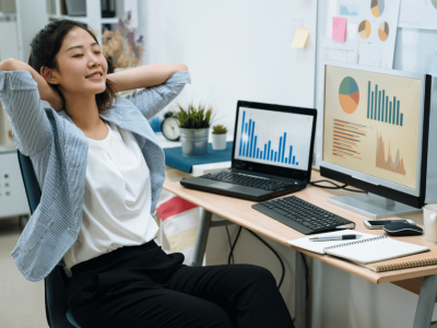 Businesswoman relaxing at desk with financial charts, highlighting factoring and invoice financing benefits for growth.