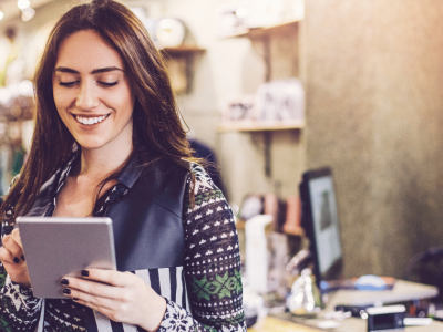 Smiling woman using a tablet in a retail store, exploring holiday loans for small business inventory and staffing needs.