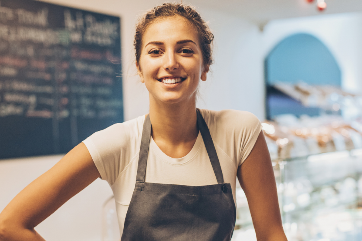 Smiling business owner in an apron, representing small business growth and loan potential in a cafe setting.