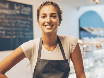 Smiling business owner in an apron, representing small business growth and loan potential in a cafe setting.