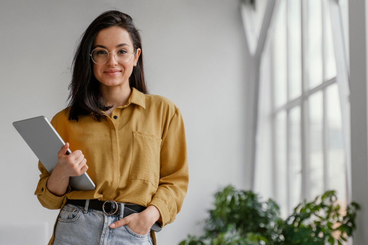 Young businesswoman holding a tablet in a bright office, emphasizing the importance of location in real estate for small businesses.