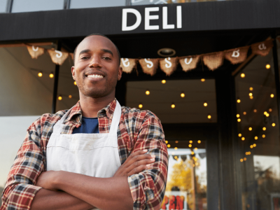 Smiling small business owner in front of deli, showcasing entrepreneurial spirit and success with business lines of credit.