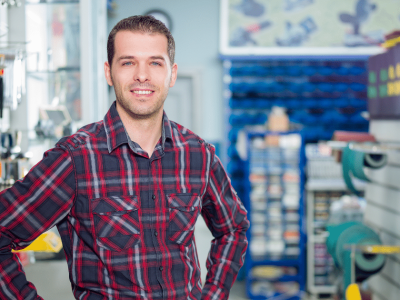 Smiling man in a plaid shirt standing in a manufacturing tools store, representing unsecured loans for manufacturing businesses.