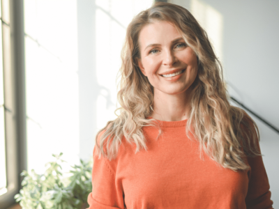 Smiling woman in an orange sweater, representing entrepreneurship in small business niches like translation and green construction.