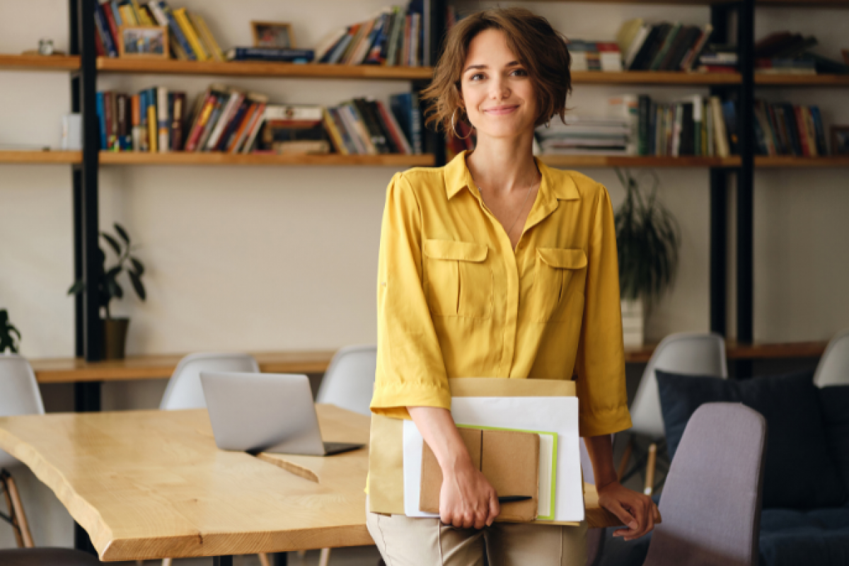 Businesswoman in a yellow shirt holding documents, representing financial empowerment and avoiding personal savings for business expenses.