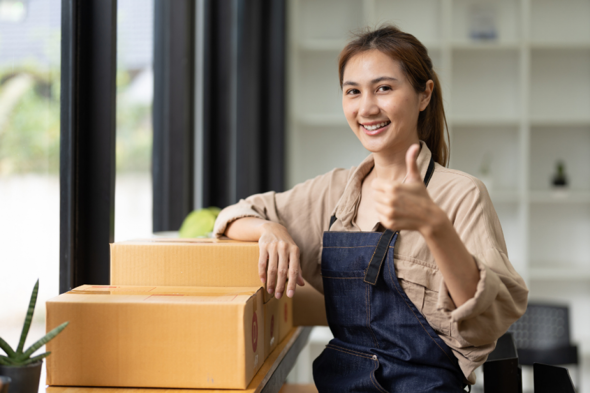 Smiling woman giving a thumbs up next to boxes, representing growth in pharmacy and medical equipment businesses.