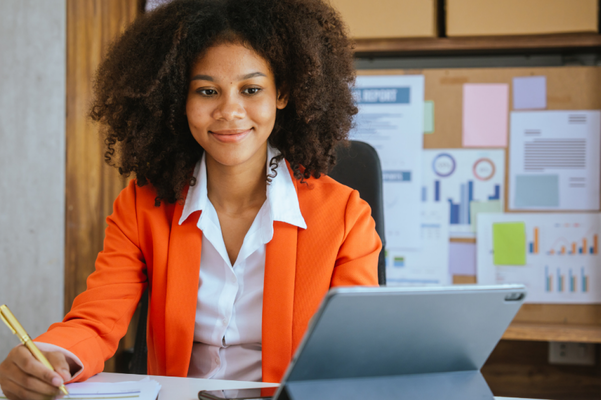 Business professional in an orange blazer managing finances with a tablet, emphasizing receivables financing solutions.