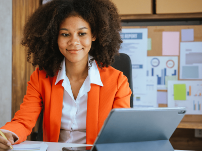 Business professional in an orange blazer managing finances with a tablet, emphasizing receivables financing solutions.