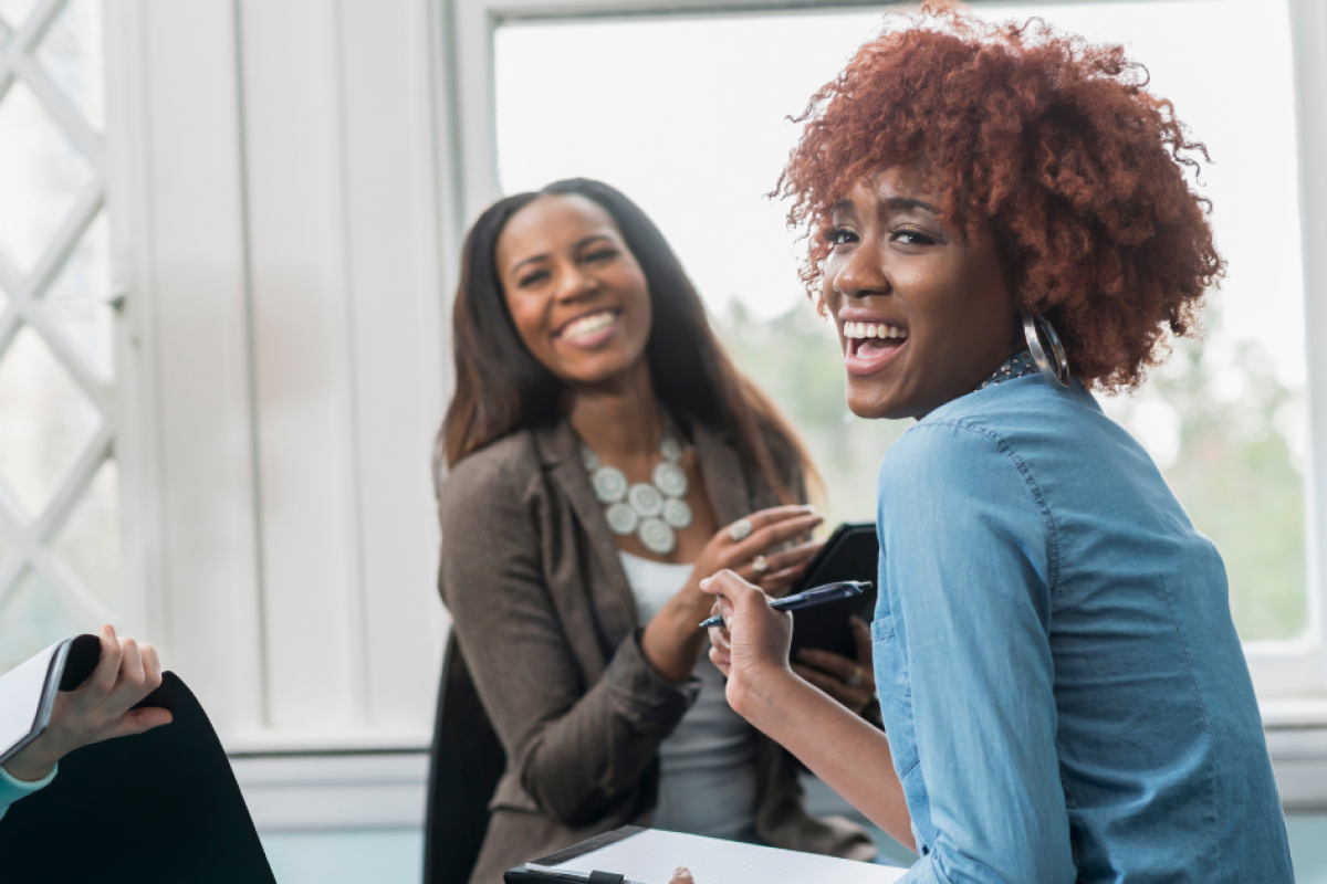 Two women smiling and engaging in a discussion, representing teamwork and support in financial recovery and credit repair strategies.