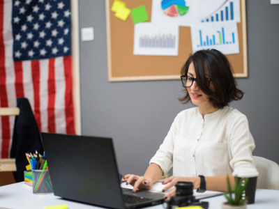 Businesswoman working on a laptop in an office with charts, emphasizing essential CEO qualities for leadership and success.