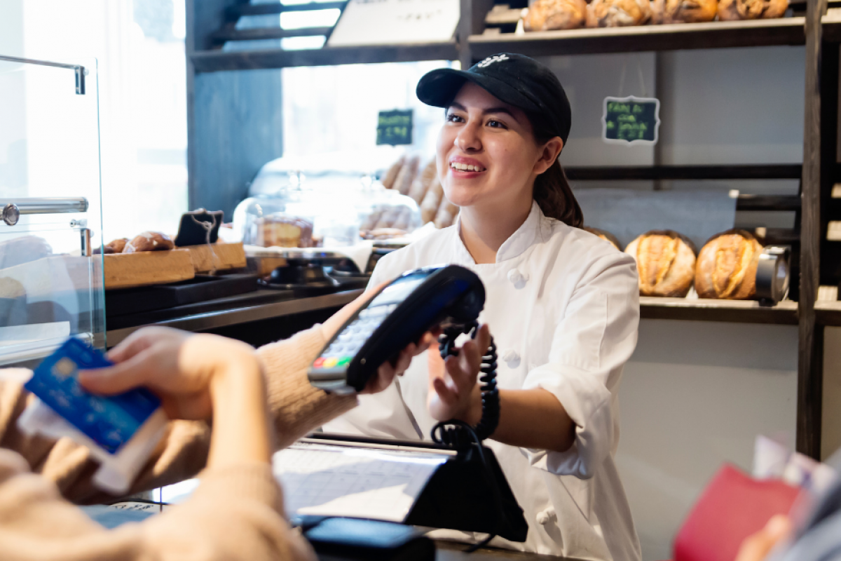 Business financing solutions for growth, featuring a cashier assisting a customer with payment in a bakery setting.