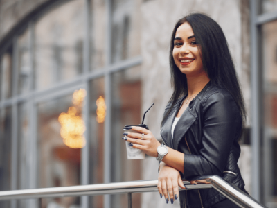 Smiling woman in a leather jacket holding a drink, representing customer engagement and inviting business atmosphere.