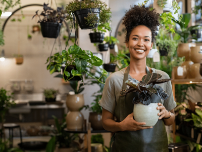 Smiling woman holding a plant in a vibrant garden center, showcasing business line of credit solutions in New Jersey.