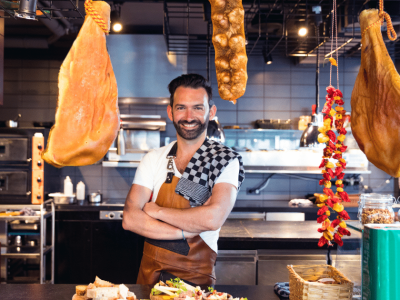 Chef in a restaurant kitchen with hanging meats and spices, showcasing effective business budget strategies for culinary success.