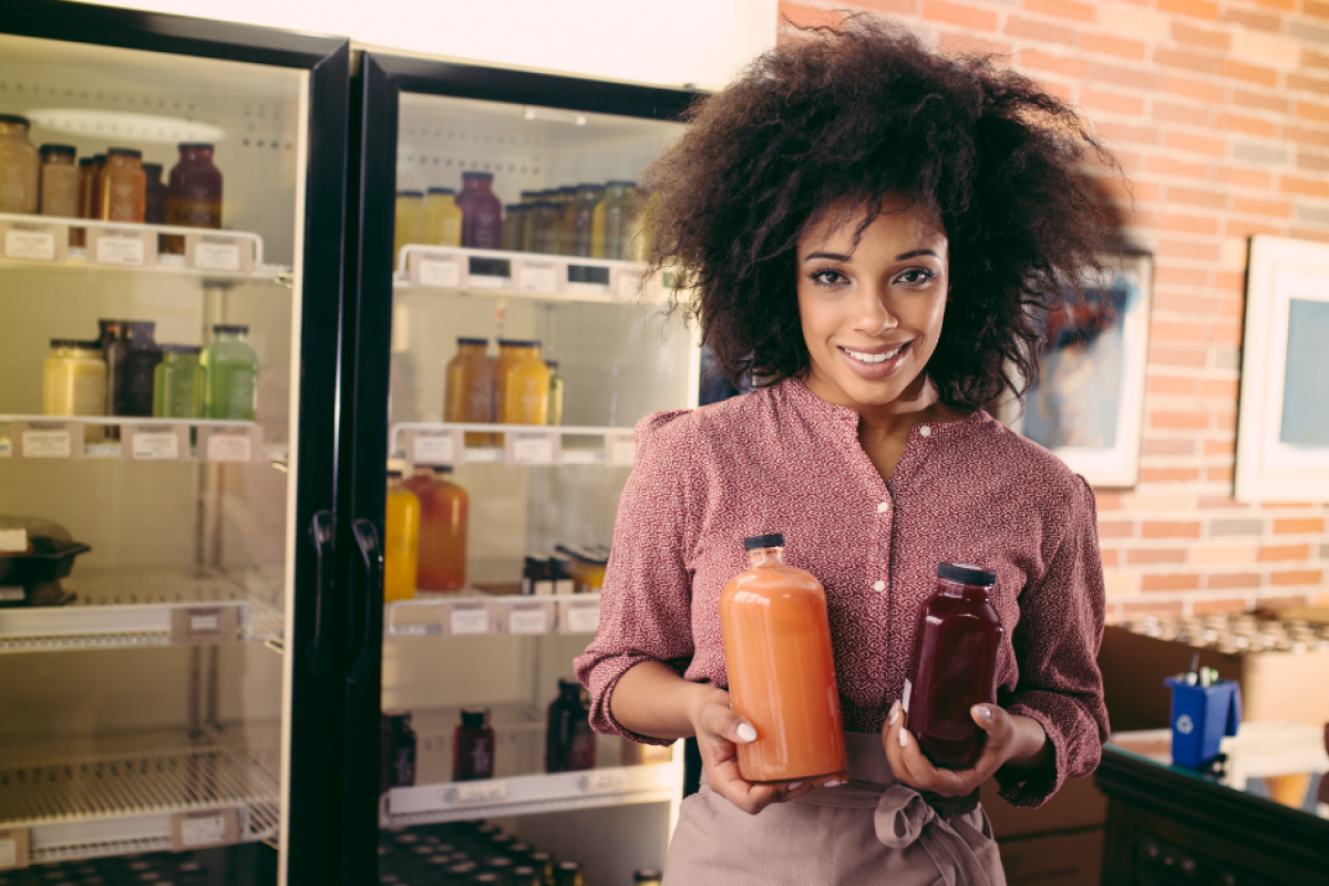 Smiling woman holding juice bottles in a small business, showcasing cost-cutting strategies for entrepreneurs.