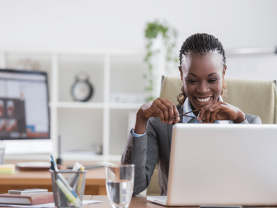 Smiling businesswoman engaging with online marketing strategies at her desk with a laptop and multiple screens.