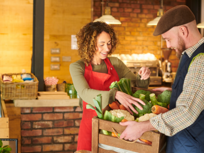 Smiling business owners exchanging fresh produce in a vibrant market, showcasing community networking and collaboration.