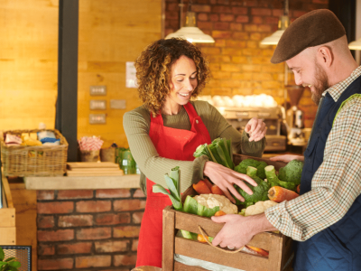 Smiling business owners exchanging fresh produce in a vibrant market, showcasing community networking and collaboration.