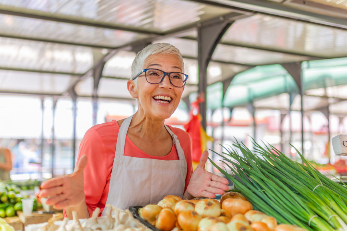 Smiling vendor at a market showcasing fresh organic produce, emphasizing customer service and community engagement.