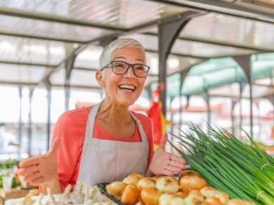 Smiling vendor at a market showcasing fresh organic produce, emphasizing customer service and community engagement.
