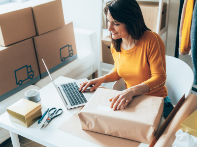 Woman managing her small business finances with packages and laptop, highlighting unsecured business loan eligibility.
