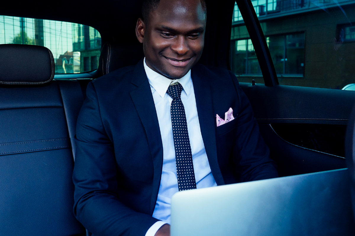 Business professional working on a laptop in a car, highlighting the importance of financial awareness and banking fees.