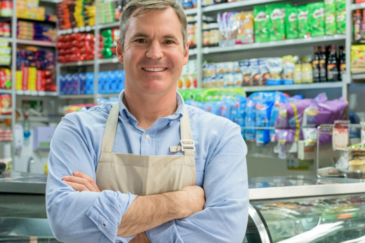 Smiling grocery store owner in apron, showcasing leadership and customer service skills in a vibrant retail environment.