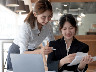 Two businesswomen discussing small business loan documents in a modern office setting, emphasizing collaboration and preparation.
