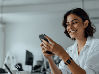 Smiling woman in a white shirt engaging with her phone, representing successful dealmaking and sales strategies.