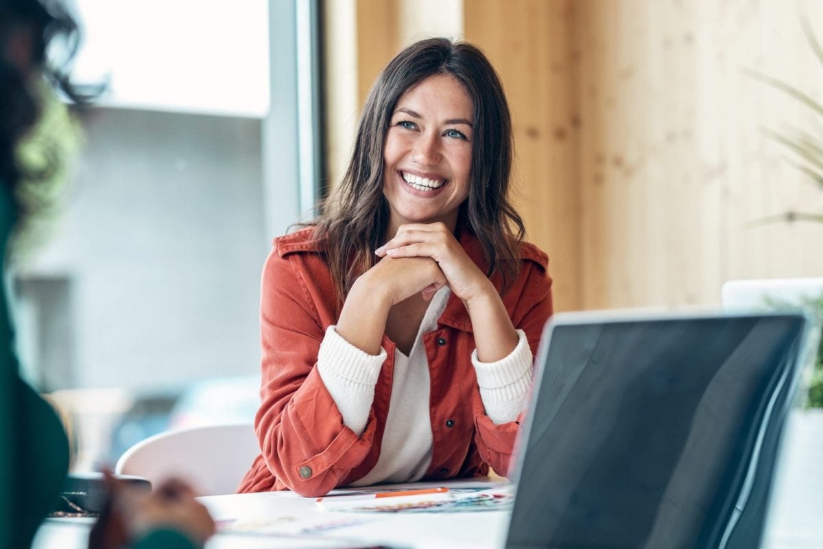 Smiling woman in a business setting discussing short-term financing options with a laptop and documents on the table.