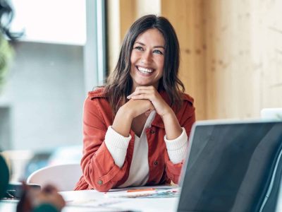 Smiling woman in a business setting discussing short-term financing options with a laptop and documents on the table.