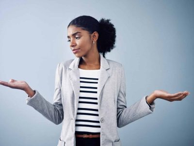 Decisions, choices and options with a young business woman comparing and weighing up different decisions with copyspace in studio against a grey background. Picking between two balanced ideas.